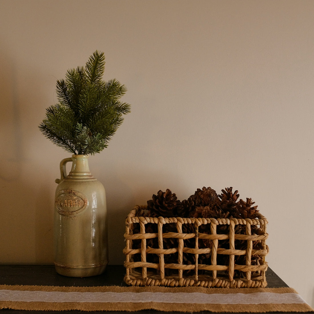 Pine sprig in jug next to basket of pinecones